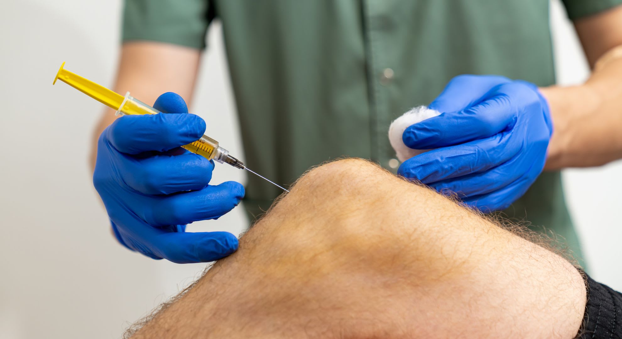 A medical professional wearing blue gloves administers a bpc 157 peptide injection into a patient's knee using a syringe.